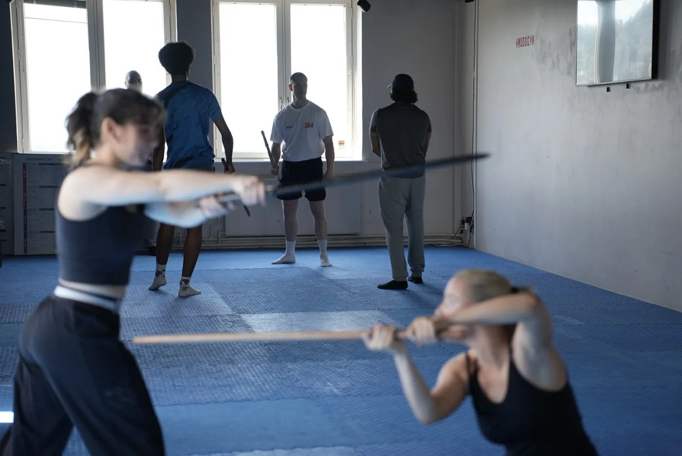 Elever som trener parøvelser med trestaver i et lyst studio