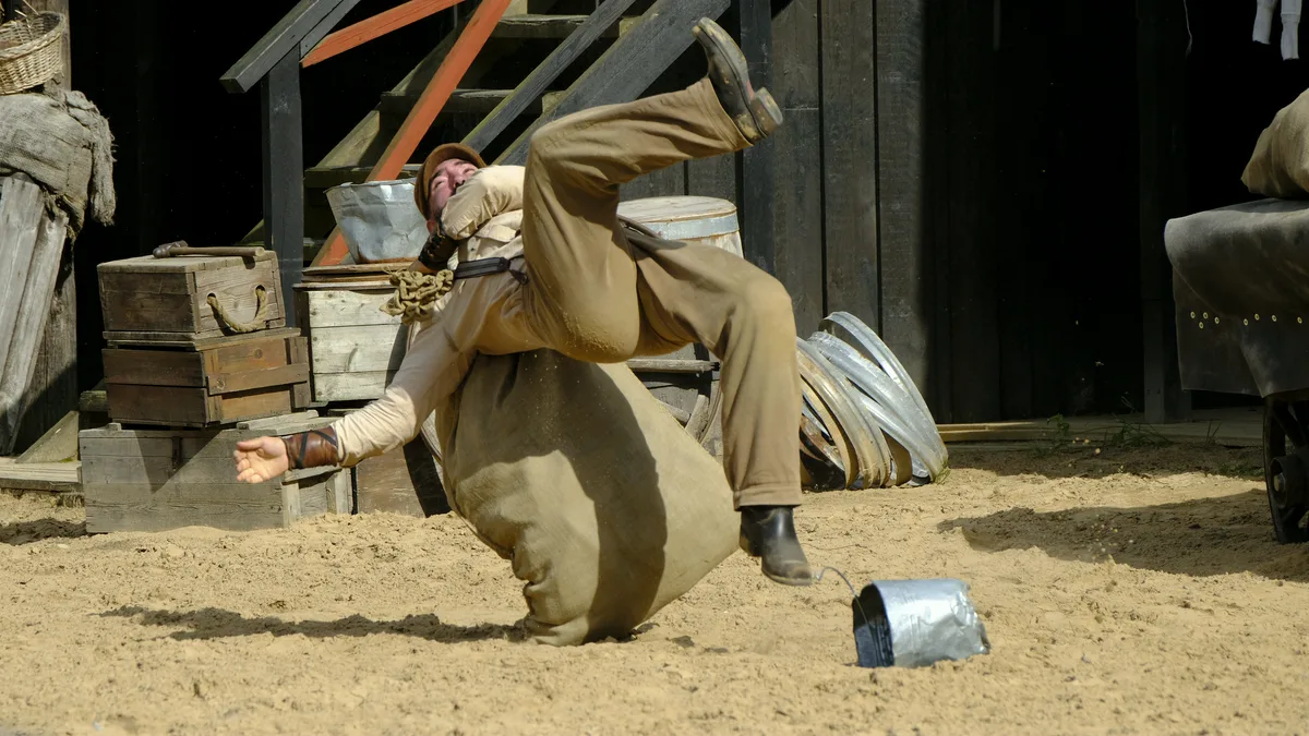 Bertan faller bakover over en sekk i sanden under et westernstuntshow